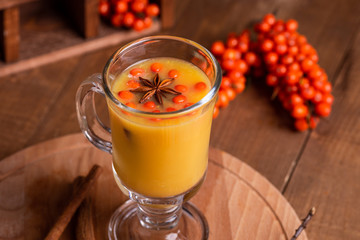 Hot beverage of sea-buckthorn berries in glass cup on wooden background. Rustic style.