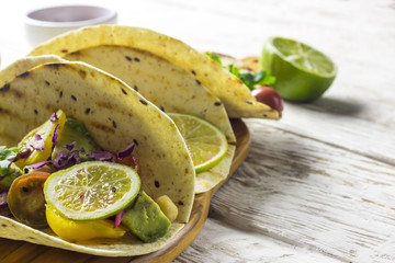 Healthy corn tortillas with chickpeas, tomatoes, avocado, fresh arugula, limes over white wooden background, top view. Healthy food, gluten-free, allergy-friendly, weight loss concept