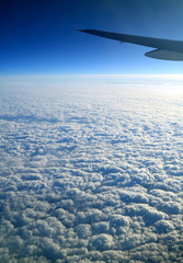 Deep blue sky and pure white clouds with airplane wing seen from plane window during the flight  