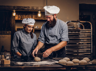 Chef teaching his assistant to bake the bread in a bakery.