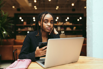 Portrait of businesswoman holding smartphone while working on laptop