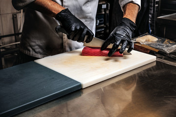 Close-up photo of a cook in uniform and gloves preparing sushi on cutting board in the kitchen.