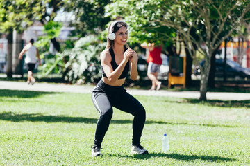 Young muscular fitness woman doing squats exercise in the park