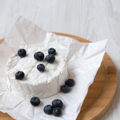 Camembert cheese in paper on bamboo board on a white wooden background, low angle view. Food for wine.
