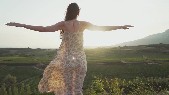 Slender woman stands on top, straightening her arms, she looks at the beautiful landscape, and her dress develops in the wind