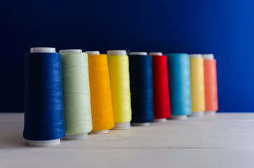 Spools of thread of different colors stand on a wooden table diagonally in front of a blue background