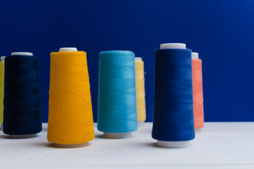 Different colored spools of sewing thread stand on a wooden table. 