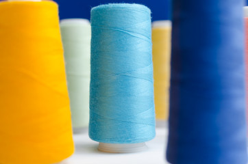 Close-up of different colored spools of sewing thread stand on a wooden table. Light blue color in focuse