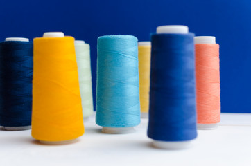 Different colored spools of sewing thread stand on a wooden table. Light blue color in focuse