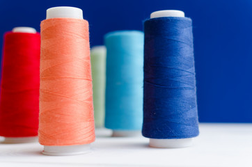Close-up of different colored spools of sewing thread stand on a wooden table