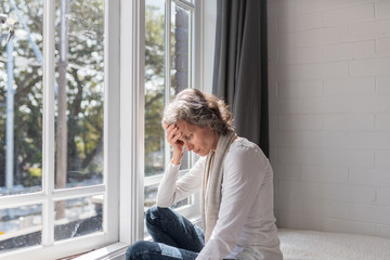 Waist up view of middle aged woman sitting by window resting head on her hand (selective focus)