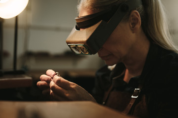 Senior jeweler examining a ring with magnifying glass - obrazy, fototapety, plakaty