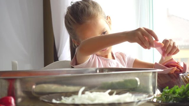 Portrait of a little girl who helps her mother in the kitchen. Daughter helps mom in pizza making 4k video. The child learns to cook food.
