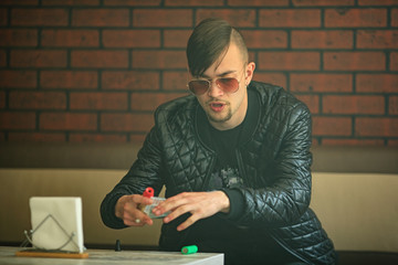 Vaping teenager. Young handsome bearded white man in a black jacket and sunglasses is smoking an electronic cigarette in vape bar.Bad habit.