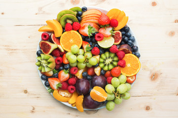 Healthy fruit platter, strawberries raspberries oranges plums apples kiwis grapes blueberries on the light wooden pine table, top view, copy space for text, selective focus