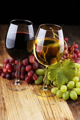 Weißwein und Rotwein in einem Glas mit Herbsttrauben auf rustikalem Hintergrund.