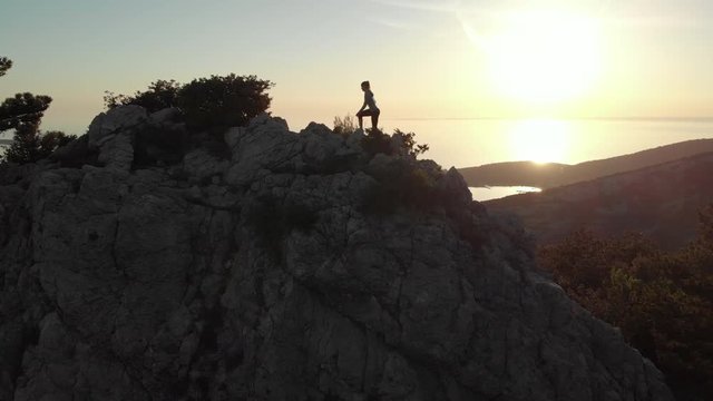 Aerial - Adult woman climbing to the top of the rock that elevates above the sea