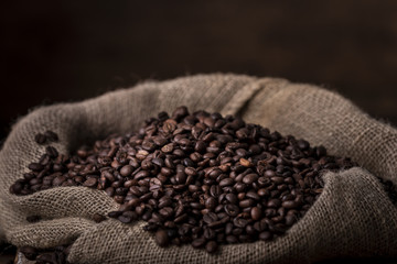 Sack of spilled fresh coffee beans on brown wooden background