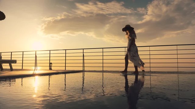 Slow motion - Beautiful shot of a woman in a long flow dress walking by the pool