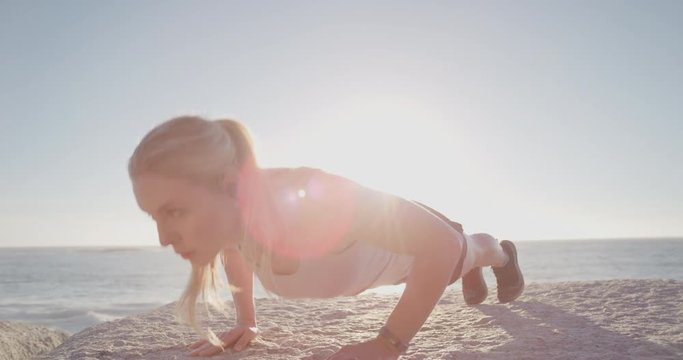 young blonde woman runner doing push ups exercise on beach at sunrise listening to music for motivation enjoying healthy fitness lifestyle wearing earphones