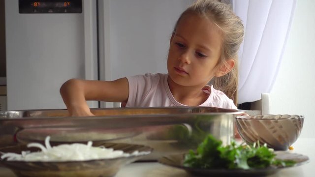 Portrait of a little girl who helps her mother in the kitchen. Daughter helps mom in pizza making 4k video. The child learns to cook food.
