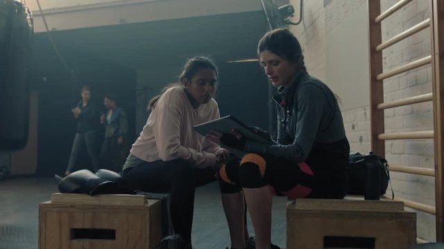 healthy woman trainer using tablet computer fitness coach sharing performance results to female athlete enjoying workout motivation in gym meeting talking together slow motion