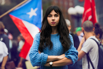 Beautiful activist woman protesting on city street with arms crossed