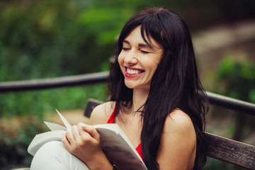 Beautiful smart woman reading a book and laughing in the green park outdoors