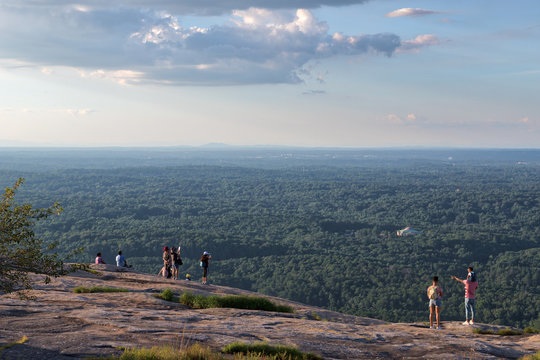 Several unidentifiable people looking out over the green trees and forests visible from the top of Stone Mountain in Georgia on a lovely summer day