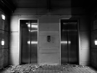 Black and white image of urban elevator doors and gray concrete walls at night,