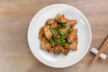 top view of stir fried chicken with black soy sauce in a ceramic dish on wooden table. asian homemade style food concept.