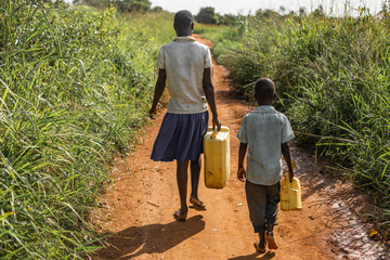 Young boy and girl walk to get water for their village, carrying jerry cans.
