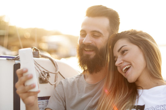 Attractive couple relaxes, taking photos and using a smartphone on a sailboat