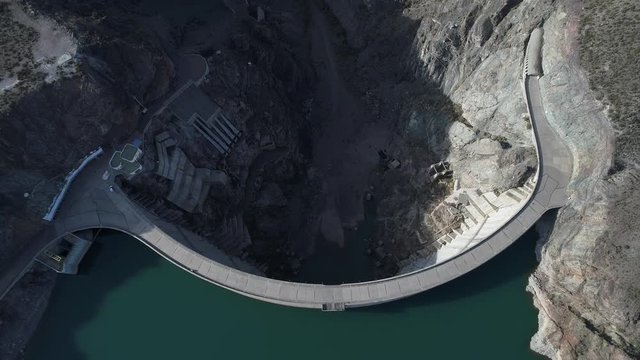 Aerial drone scene top view of semicircular Agua de Toro Dam at San Rafael, Mendoza, Cuyo Argentina. Camera moving backwards and punning up to the horizon. First light of the day.