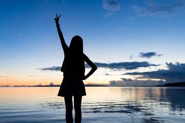 Fototapeta premium Silhouette of woman showing victory sign with the background of sea and sunset