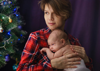 Family celebration. Portrait of young mother and newborn baby. In background Christmas tree. Happiness of motherhood.