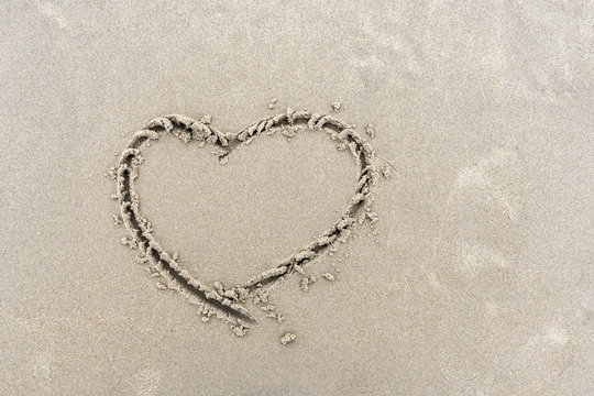 Symbol of heart written by hand on sand of beach with copy space