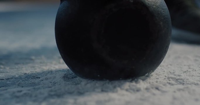 fitness man training bodybuilding using kettlebell weightlifting intense strength exercise dropping heavy weight on chalk powder in gym close up slow motion