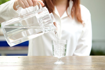 Beautiful woman pouring pure water from a pitcher. Take a glass of water and drink water to moisturize. Health concept