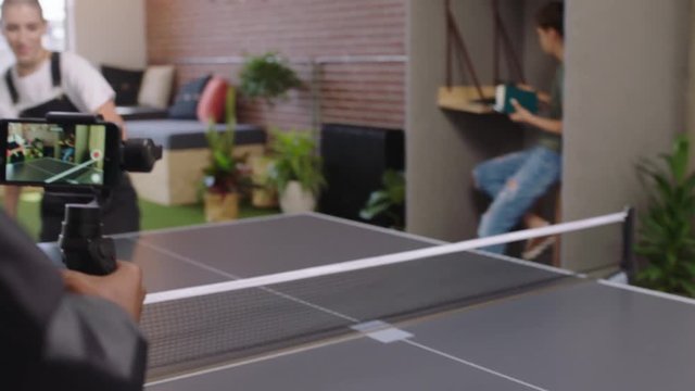business people playing ping pong in office diverse students enjoying competitive fun colleague using smartphone taking video sharing game on social media modern workplace recreation