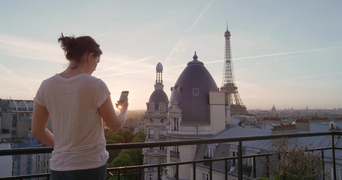 happy woman using smartphone taking photo enjoying sharing summer vacation experience in paris photographing beautiful sunset view of eiffel tower on balcony