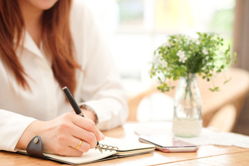 Hands of a working beautiful woman are writing a note on her booklet at work in the morning, a...