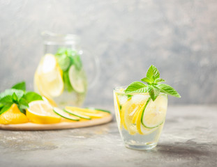 A refreshing cocktail of mahito with pieces of fresh lemon and lime and mint leaves with ice in a glass on a gray background. Summer drink lemonade.