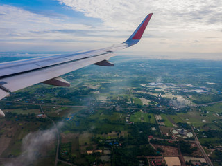 Wing of the plane Fly over the city in Thailand. In the blue sky and white clouds.
