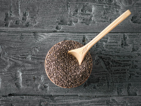 Wooden spoon in a bowl with black Chia seeds on a wooden table. The view from the top. Flat lay.