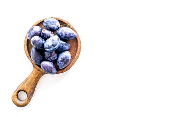 Plums on dinning table. Fresh raw purple plum in wooden bowl on white background top view space for text