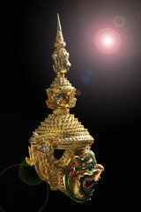 A giant golden mask in Thai art style with a light fixture from the top.