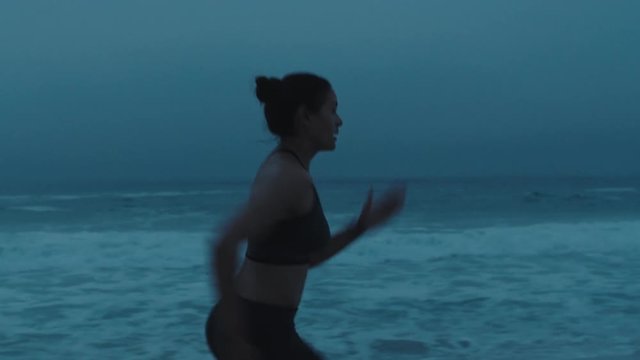 strong young woman running on stormy beach sprinting fast exercising cardio workout training focused female athlete runner in cloudy seaside background
