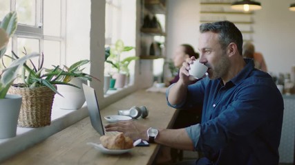 mature businessman using laptop computer in cafe sharing successful business ideas on social media independent entrepreneur drinking coffee working enjoying relaxed lifestyle