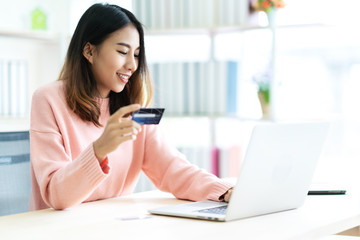 Young attractive asian woman holding credit card sitting at table typing keyboard on laptop...